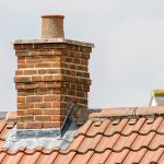 Brick chimney stack on modern contemporary house roof top. Urban housing estate tiled roof in close-up.